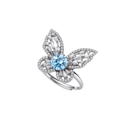 Sterling silver ring with blue moissanite center stone surrounded by clear stones in butterfly wing pattern on white background
