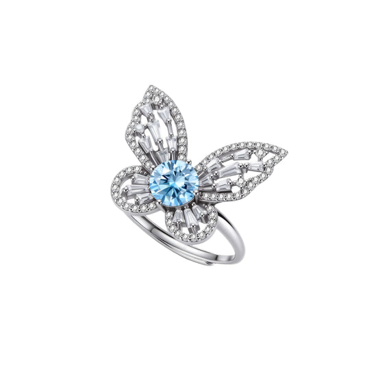 Sterling silver ring with blue moissanite center stone surrounded by clear stones in butterfly wing pattern on white background