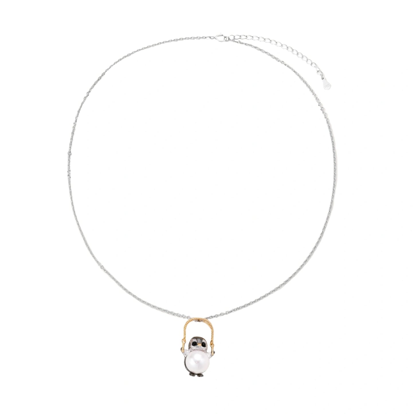 Whimsical owl pendant holding a white pearl on a gold swing, rhodium-plated silver chain on cream background.