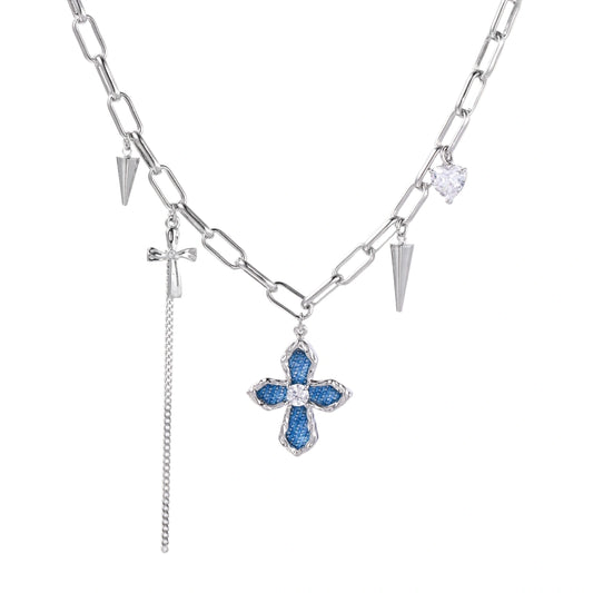 White gold plated chain necklace with blue textured cross pendant, spike charms, and mini cross detail on beige background
