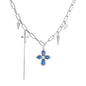 White gold plated chain necklace with blue textured cross pendant, spike charms, and mini cross detail on beige background