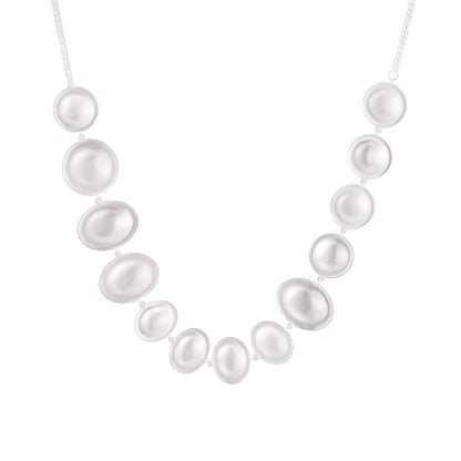 Graduated pearl-finish silver discs forming an organic bubble bib necklace on delicate chain against cream background.