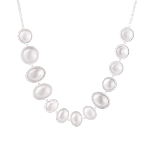 Graduated pearl-finish silver discs forming an organic bubble bib necklace on delicate chain against cream background.