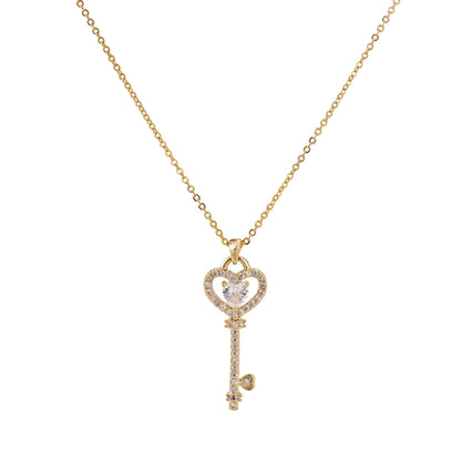 Delicate gold key pendant with heart-shaped bow and crystal pavé detailing on fine chain against cream background.