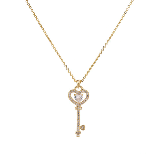 Delicate gold key pendant with heart-shaped bow and crystal pavé detailing on fine chain against cream background.