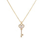 Delicate gold key pendant with heart-shaped bow and crystal pavé detailing on fine chain against cream background.