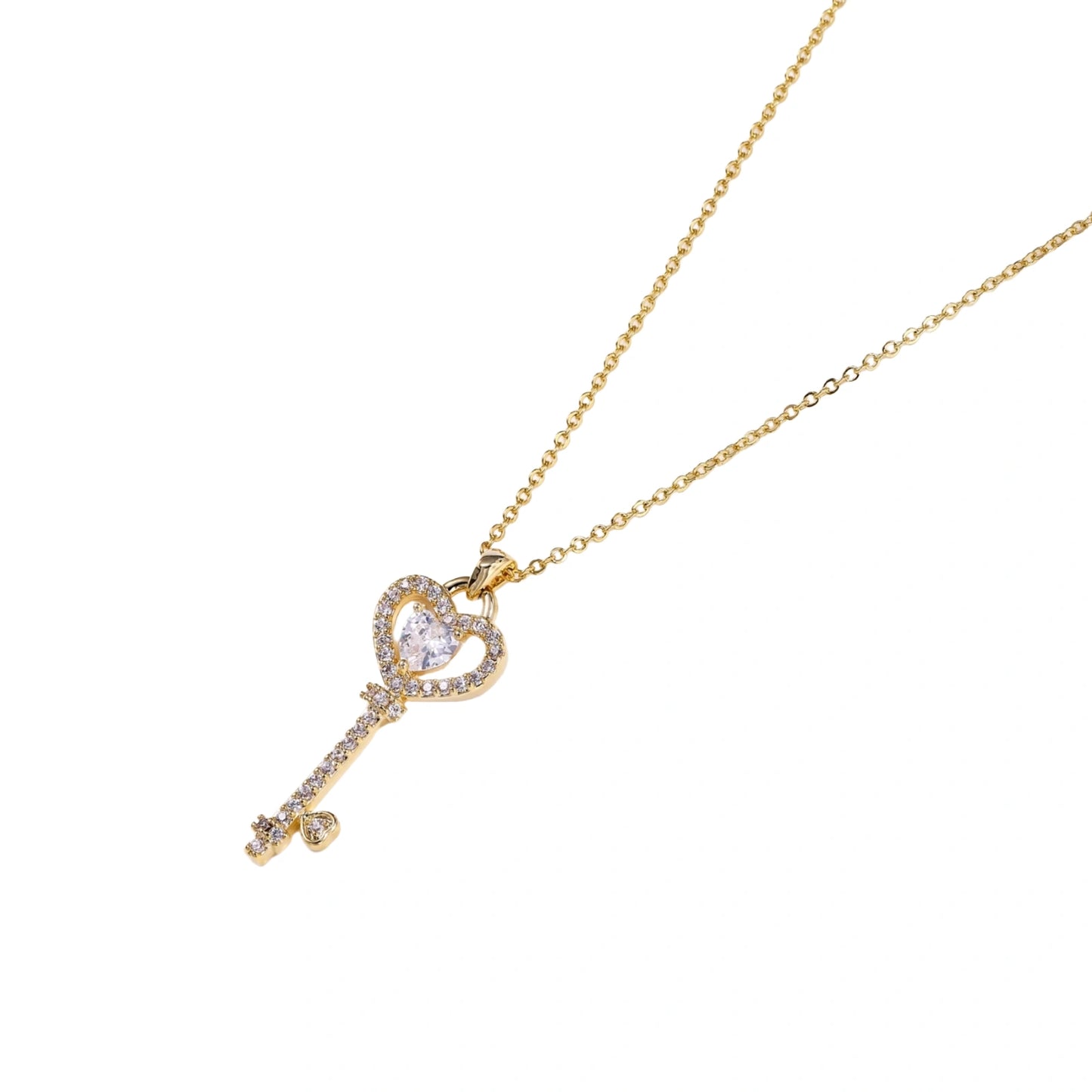 Delicate gold key pendant with heart-shaped bow and crystal pavé detailing on fine chain against cream background.