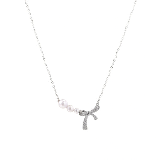 Delicate white gold plated necklace with freshwater pearls and sparkly crystal bow pendant on white background